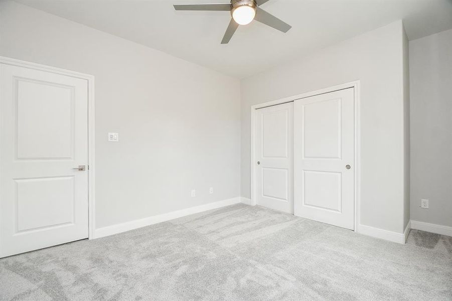 This is a clean, secondary  bedroom featuring plush carpeting, neutral walls, a ceiling fan, and a double-door closet providing ample storage.