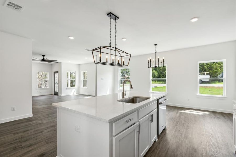 Kitchen with light stone counters, dark hardwood / wood-style floors, ceiling fan with notable chandelier, a center island with sink, and sink
