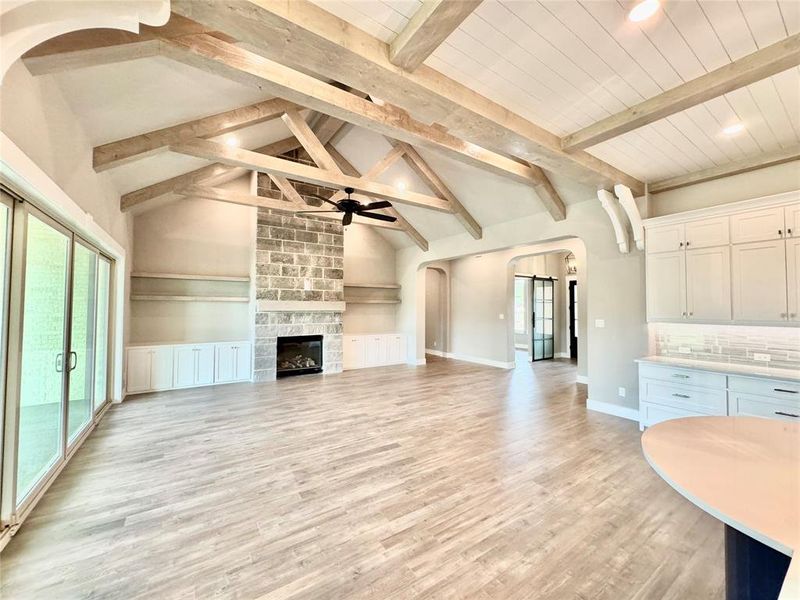 Unfurnished living room featuring a fireplace, light wood-type flooring, lofted ceiling with beams, and ceiling fan