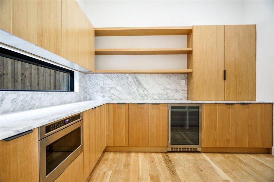 Kitchen featuring wine cooler, light wood-type flooring, oven, light brown cabinetry, and light stone countertops