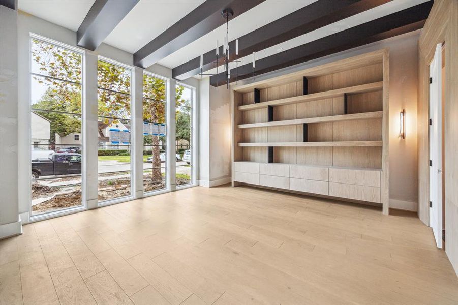 Off the entrance of the home is a Formal Library with Floor to Ceiling Windows, Boxed Beamed Ceiling, White Oak  Shelving with Stone Dividers and Drawers.  There are also sconces on each side of the Cabinet.