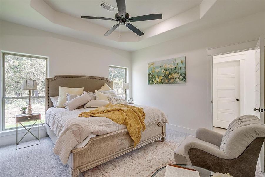 Bedroom with light carpet, a raised ceiling, and ceiling fan