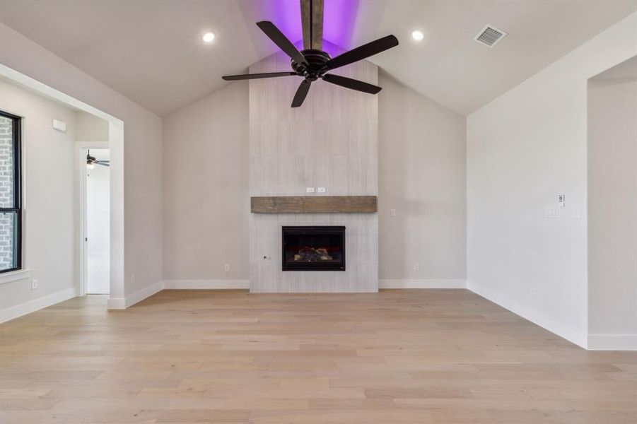 Unfurnished living room featuring ceiling fan, a large fireplace, and light hardwood / wood-style floors