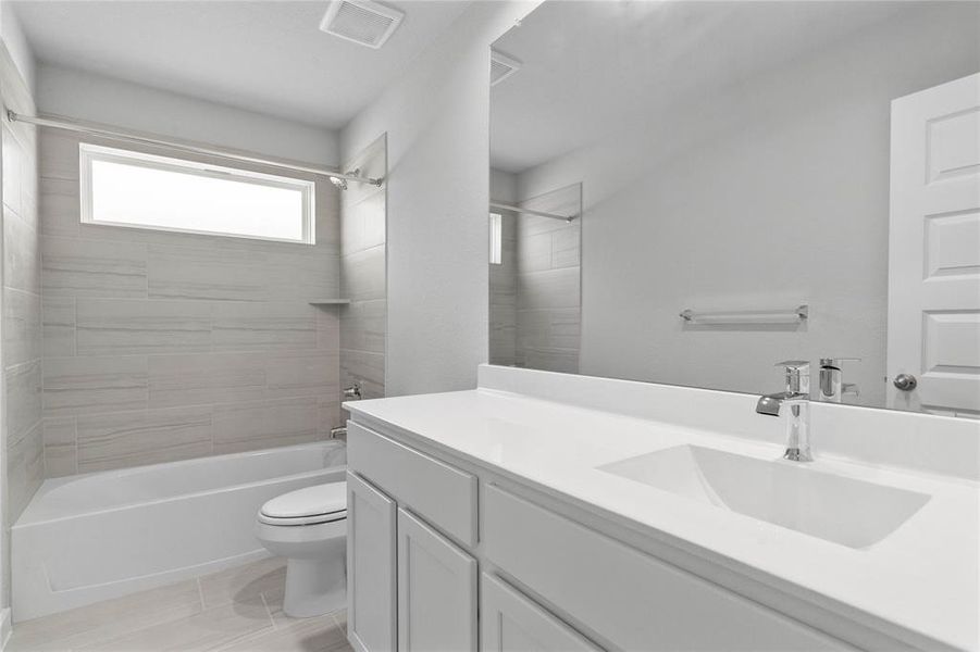 Secondary bath features tile flooring, tub/shower combo with tile surround, white stained wood cabinets, beautiful light countertops, mirror, sleek fixtures and modern finishes.