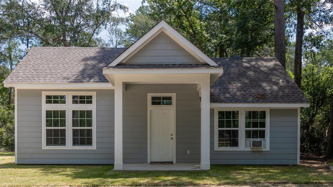 Cozy single-story home with a blue exterior, white trim, and a gabled roof, featuring a covered entryway and multiple windows, nestled among trees.