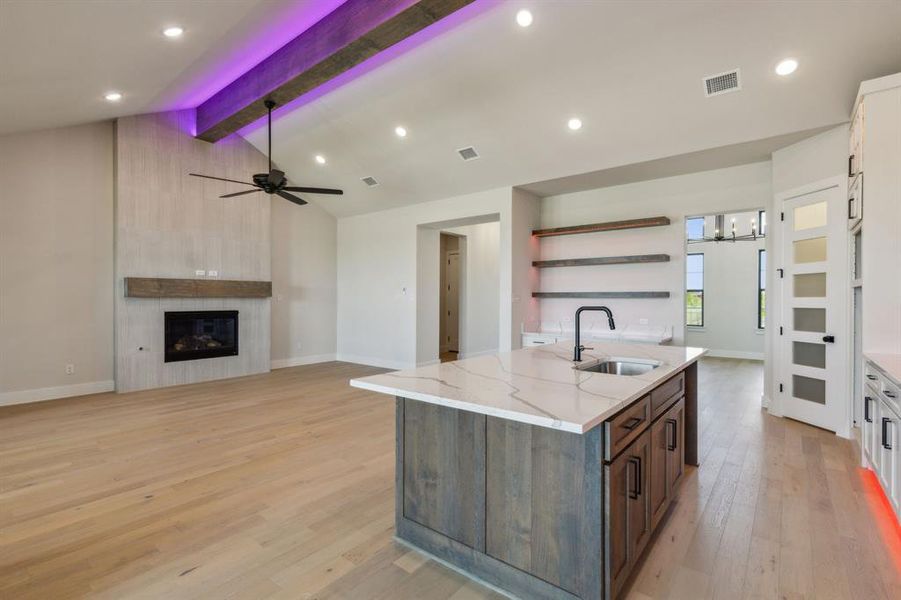 Kitchen featuring light hardwood / wood-style flooring, a large fireplace, sink, light stone countertops, and vaulted ceiling with beams