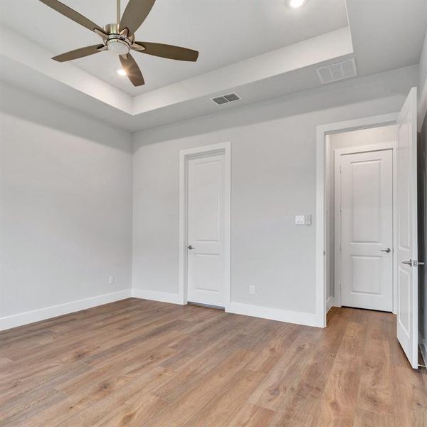 Unfurnished bedroom featuring a tray ceiling, light wood-type flooring, and ceiling fan