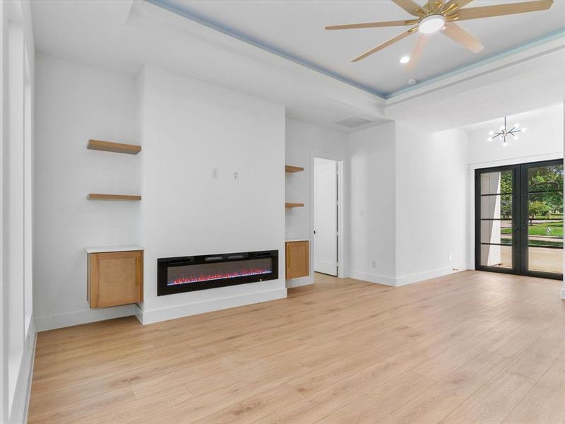 Unfurnished living room with light hardwood / wood-style flooring, a raised ceiling, and ceiling fan with notable chandelier