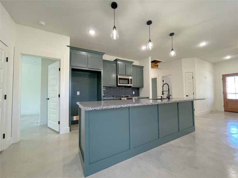 Kitchen featuring a center island with sink, decorative backsplash, sink, light stone countertops, and decorative light fixtures