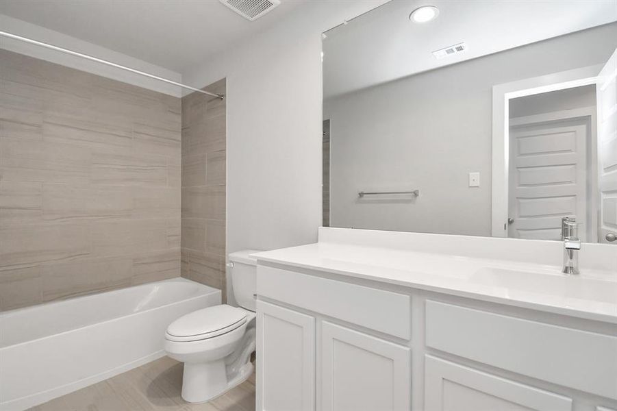 Secondary bath features tile flooring, bath/shower combo with tile surround, light stained wood cabinets, beautiful light countertop. Sample photo, actual color and selections can vary.