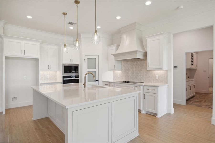 Kitchen featuring a center island with sink, white cabinets, sink, custom exhaust hood, and pendant lighting