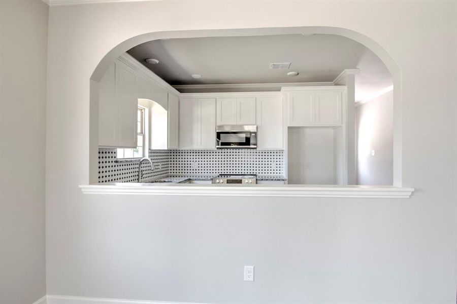 Kitchen with backsplash, white cabinets, sink, and range