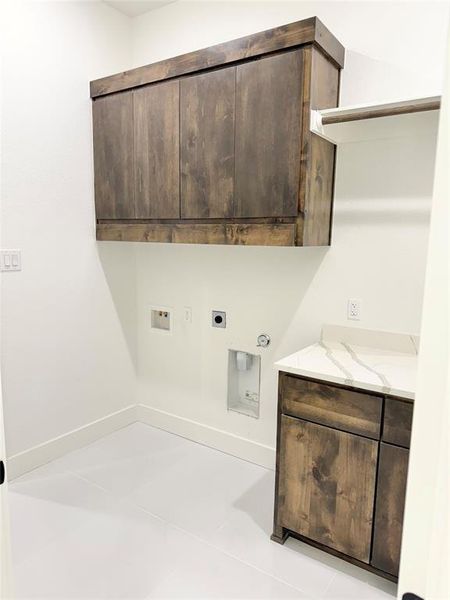 Washroom featuring hookup for a washing machine, hookup for an electric dryer, light tile patterned flooring, hookup for a gas dryer, and cabinets