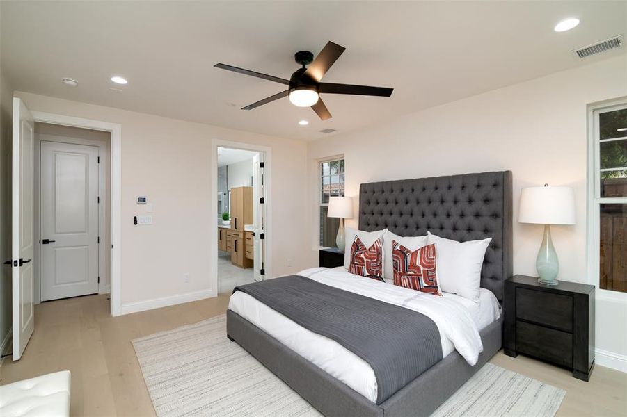 Bedroom with light hardwood / wood-style flooring, ceiling fan, multiple windows, and connected bathroom