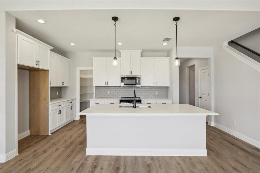 Kitchen with white cabinetry, light hardwood / wood-style flooring, and an island with sink