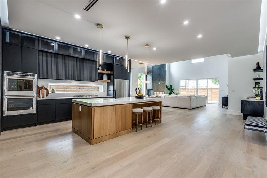 Kitchen with stainless steel appliances, light wood-type flooring, pendant lighting, a breakfast bar, and a kitchen island with sink