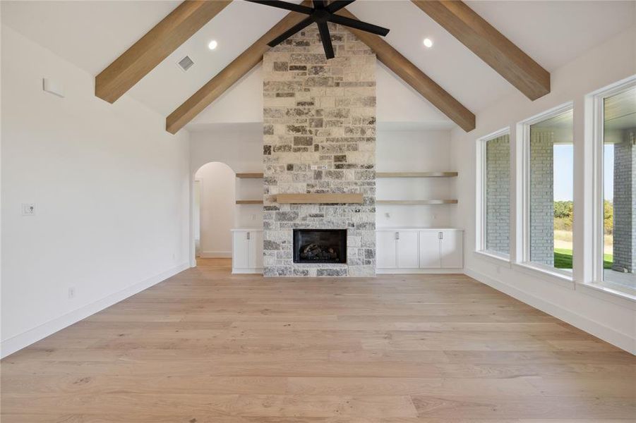 Unfurnished living room with a stone fireplace, beamed ceiling, high vaulted ceiling, and light hardwood / wood-style floors