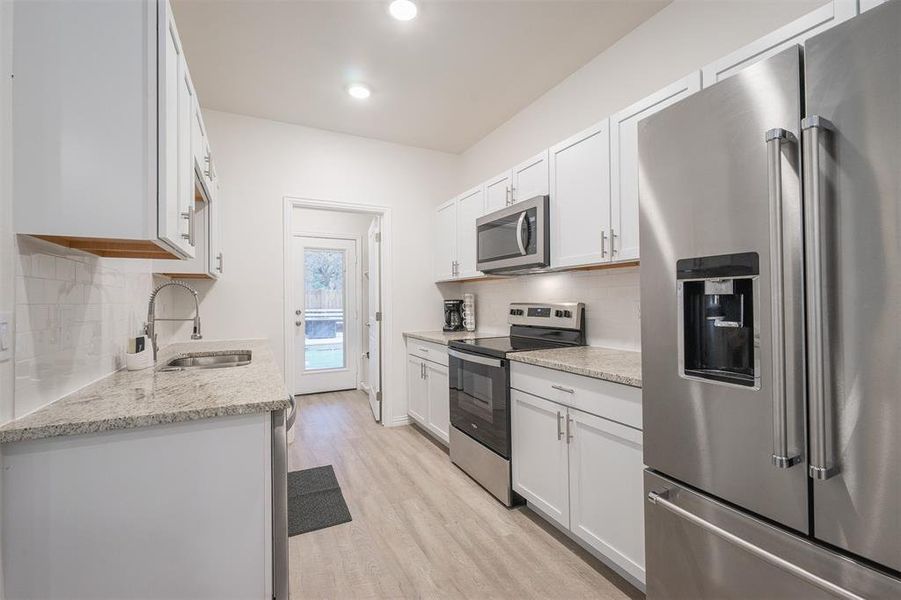 Kitchen featuring light stone counters, white cabinets, sink, stainless steel appliances, and light wood-type flooring