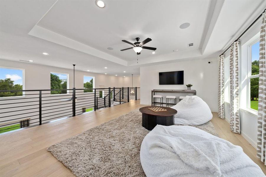 Game room with light hardwood / wood-style floors, a tray ceiling, and ceiling fan