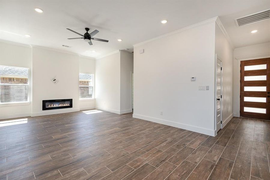 Unfurnished living room featuring a healthy amount of sunlight, crown molding, dark hardwood / wood-style floors, and ceiling fan