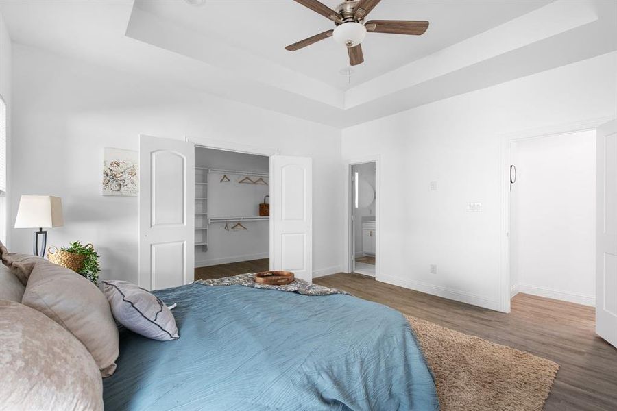 Bedroom with connected bathroom, dark hardwood / wood-style flooring, ceiling fan, a closet, and a tray ceiling