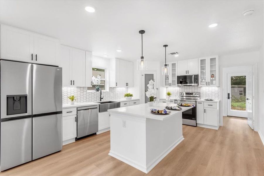 Kitchen with stainless steel appliances, light hardwood / wood-style floors, white cabinets, and sink