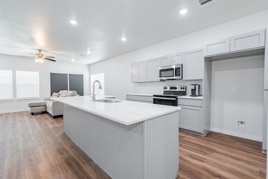 Kitchen featuring dark hardwood / wood-style floors, stainless steel appliances, sink, and a center island with sink