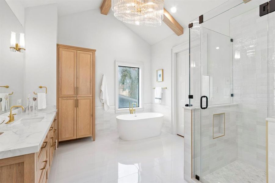 Primary Bathroom features a large glass encased walk-in shower, separate soak tub, dual vanities, arched ceilings w/ beam detail & custom built linen cabinetry.