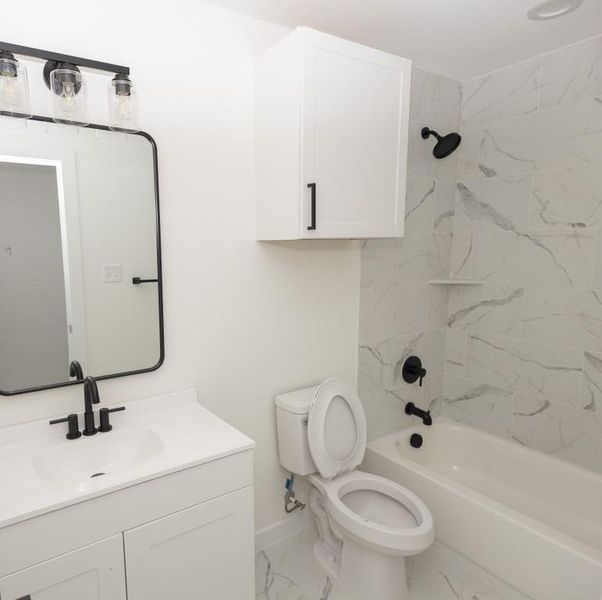 Full bathroom with tile floors, vanity with extensive cabinet space, toilet, and tiled shower / bath combo