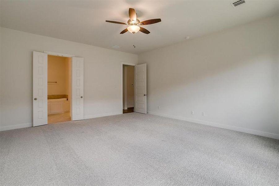 Unfurnished bedroom with ceiling fan, connected bathroom, and light colored carpet