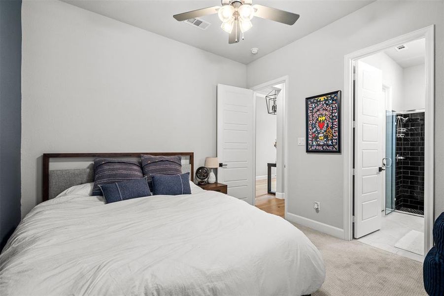 Bedroom with ceiling fan, a walk in closet, connected bathroom, and light colored carpet