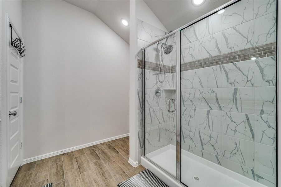 Bathroom featuring a shower with shower door, vaulted ceiling, and hardwood / wood-style flooring