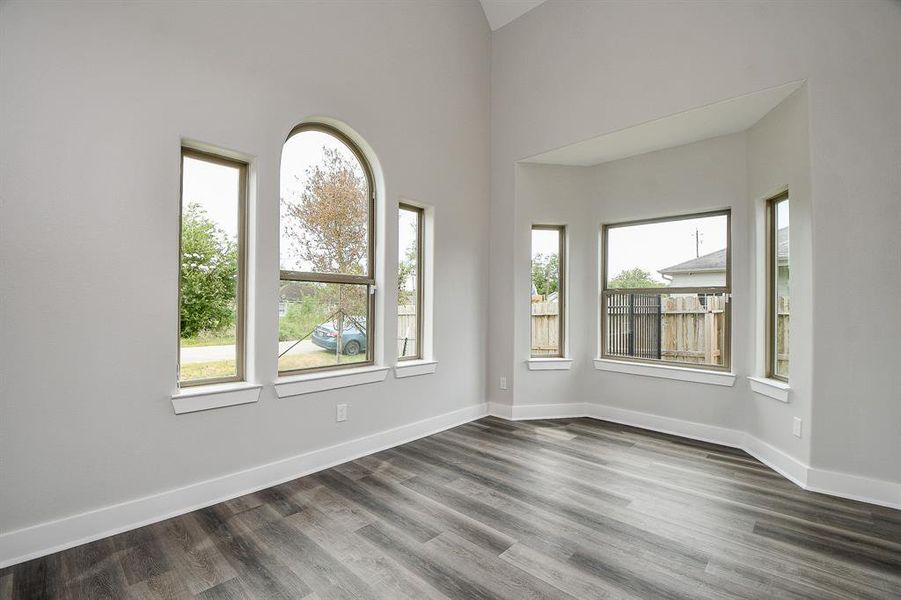 This  bright, living room with high ceilings, featuring three arched windows providing ample natural light, and a modern grey wood-look flooring.