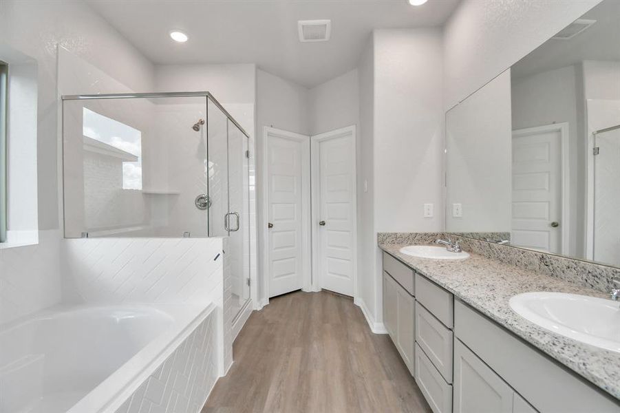 Enter a tranquil retreat in your primary bathroom. Enjoy the spacious walk-in shower, elegantly tiled, relax in a separate garden tub with custom details, and enhance your daily routines at the stylish vanity featuring double sinks, light countertops, modern hardware, and bright recessed lighting.