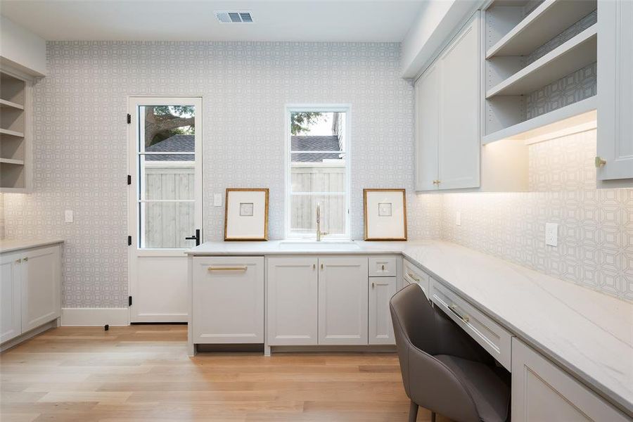 Kitchen with light hardwood / wood-style floors, light stone countertops, white cabinets, backsplash, and sink