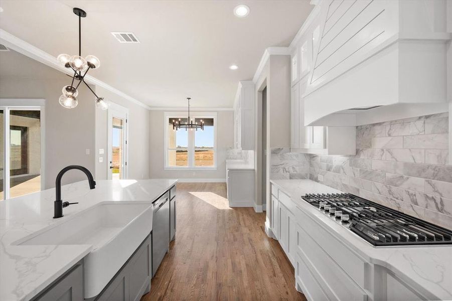 Kitchen with pendant lighting, an inviting chandelier, light wood-type flooring, white cabinetry, and appliances with stainless steel finishes