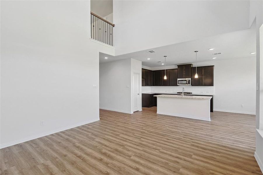 Kitchen featuring hanging light fixtures, dark brown cabinetry, light hardwood / wood-style floors, a towering ceiling, and a kitchen island with sink