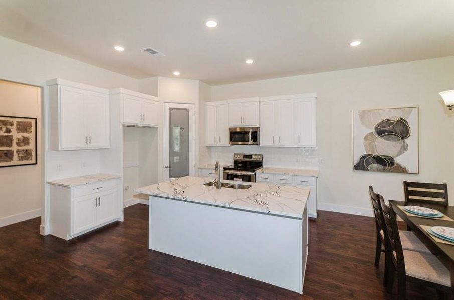 Kitchen with a kitchen island with sink, white cabinetry, stainless steel appliances, light stone counters, and dark hardwood / wood-style floors