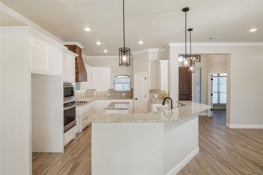 Kitchen with decorative backsplash, white cabinets, pendant lighting, and stainless steel oven