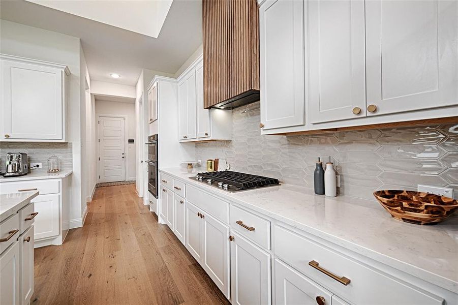 Kitchen with decorative backsplash, white cabinetry, appliances with stainless steel finishes, and light wood-type flooring