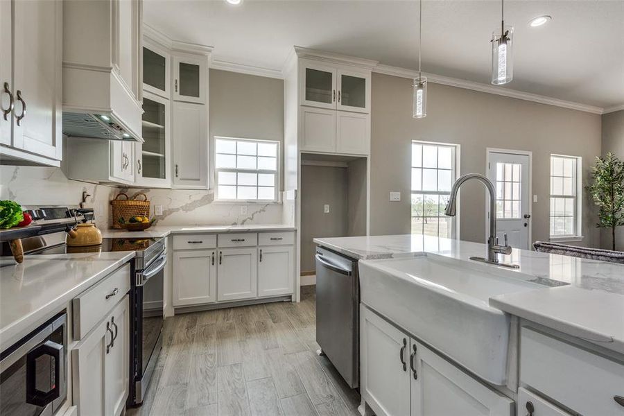 Kitchen with decorative light fixtures, premium range hood, appliances with stainless steel finishes, and white cabinetry