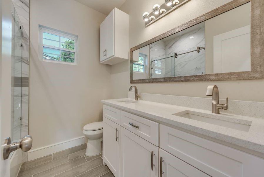 Bathroom with double sink, a shower with shower door, tile floors, toilet, and large vanity