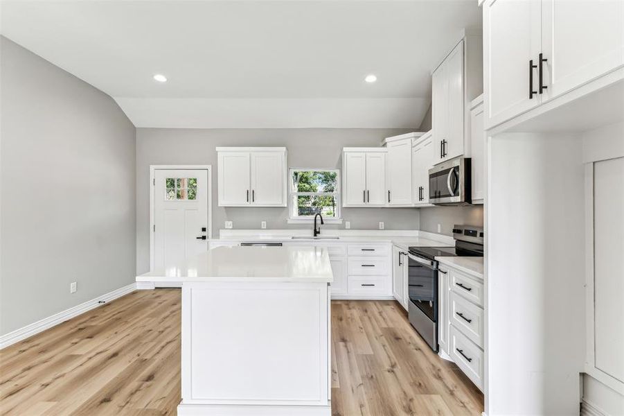 Kitchen featuring a kitchen island, stainless steel appliances, sink, light wood-type flooring, and white cabinets