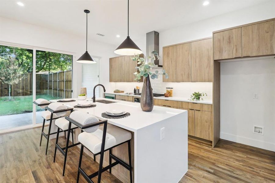 Kitchen with sink, a kitchen island with sink, decorative light fixtures, and wood-type flooring