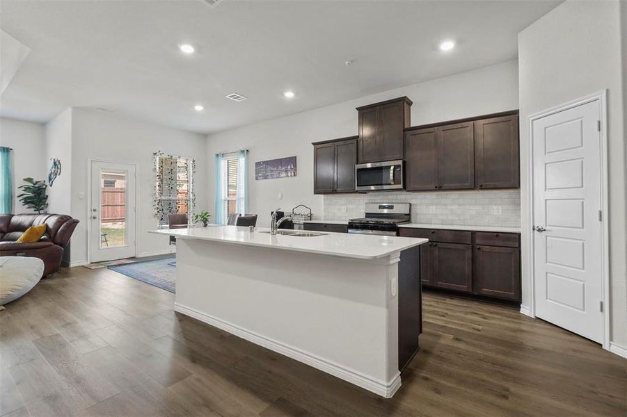 Kitchen featuring dark hardwood / wood-style flooring, appliances with stainless steel finishes, a kitchen island with sink, dark brown cabinets, and backsplash
