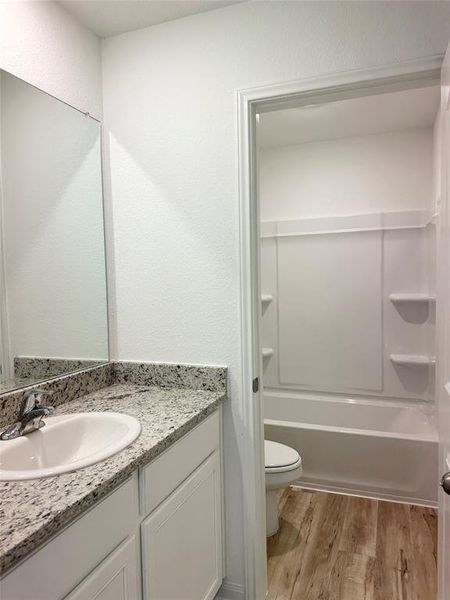 Secondary bathroom includes granite counters, designer white cabinetry and luxury vinyl plank flooring.