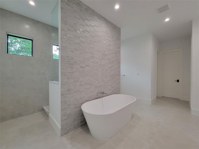 Primary bathroom with free standing Woodbridge soaking tub with floor to ceiling glass tile wall.