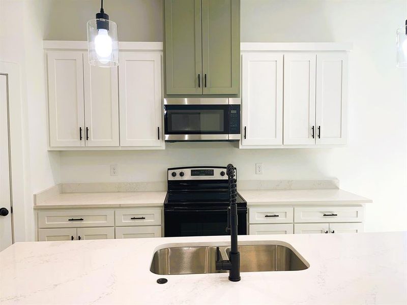 Kitchen with sink, white cabinets, pendant lighting, appliances with stainless steel finishes, and light stone counters