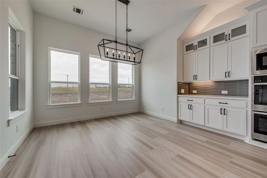 Kitchen with light hardwood / wood-style floors, white cabinets, backsplash, and pendant lighting