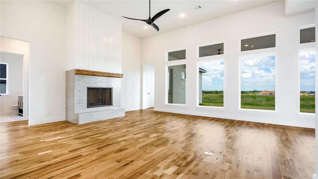 Unfurnished living room featuring a healthy amount of sunlight, a brick fireplace, ceiling fan, and light wood-type flooring